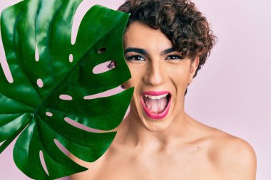 Genç adam yeşil bitki yaprağını elinde tutarak makyaj yapıyor. Güzel bir yüze yakın. Çılgınlığı kutluyor ve başarı için hayrete düşüyor.. 