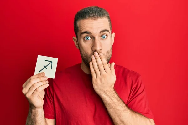 Young Caucasian Man Holding Paper Sagittarius Zodiac Sign Covering Mouth — Fotografia de Stock