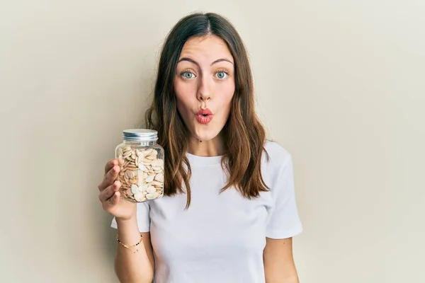 Young Brunette Woman Holding Pumpkin Seeds Scared Amazed Open Mouth — Stock Fotó