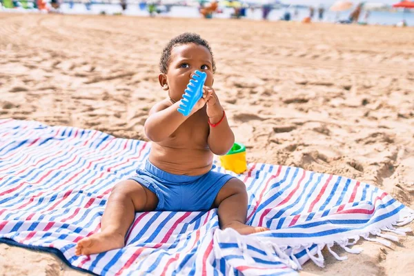 愛らしいアフリカ系アメリカ人の幼児はおもちゃで遊んでいます砂の上に座ってビーチ — ストック写真