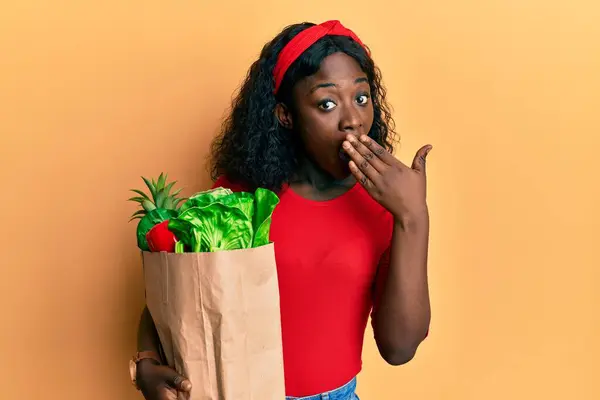Beautiful African Young Woman Holding Paper Bag Groceries Covering Mouth — Stockfoto