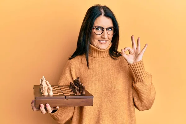 Middle Age Brunette Woman Holding Chess Board Doing Sign Fingers — Foto de Stock