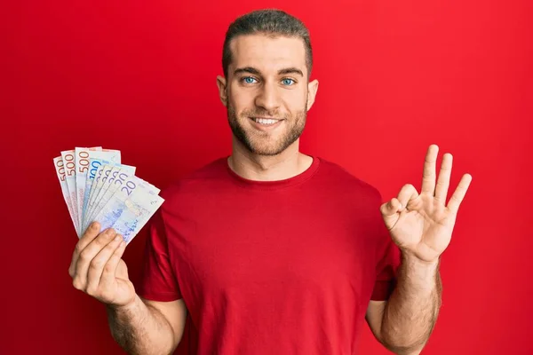 Young Caucasian Man Holding Swedish Krona Banknotes Doing Sign Fingers — Stok fotoğraf