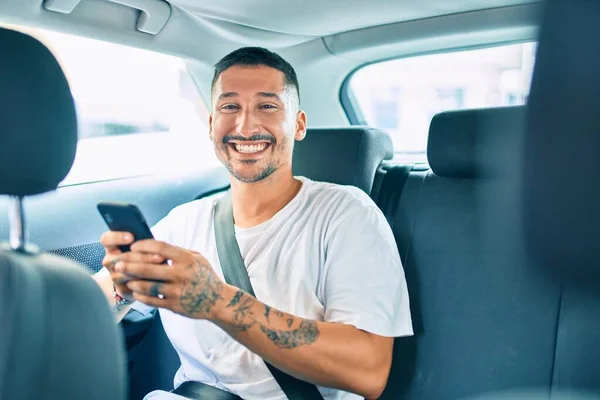 若いヒスパニック系の男は車の上に座ってスマートフォンを使用して幸せな笑顔 — ストック写真