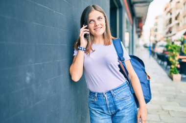 Genç ortadoğulu kız gülümseyerek üniversitenin kampüsünde akıllı telefondan konuşarak mutlu oluyor..