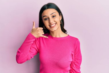 Gündelik kıyafetler giymiş, gülümseyen, el ve parmaklarıyla telefon hareketi yapan, telefonda konuşur gibi genç İspanyol bir kadın. iletişim kavramları. 