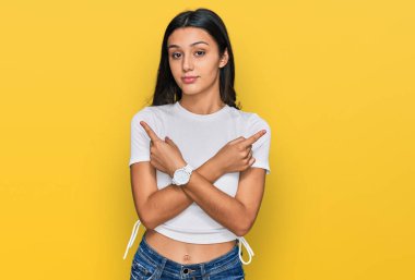 Gündelik beyaz tişört giyen genç İspanyol kız iki tarafı da parmaklarıyla işaret ediyor, farklı yönlerde. 