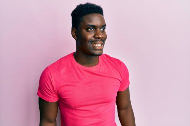 Yakışıklı, pembe tişört giyen, rahat bir görünüm takınan, doğal yüzlü, kendine güvenen bir gülümseme takınan siyah bir adam.. 