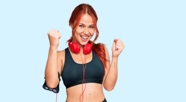 Genç kızıl saçlı kadın spor kıyafetleri giyiyor ve kulaklık takıyor. Gururla bağırıyor, zaferi kutluyor ve kollarını kaldırarak başarıyı kutluyor. 