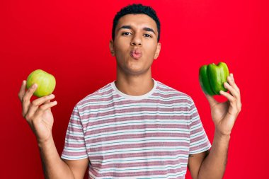Genç Arap adam elinde yeşil elma ve biber tutarak kameraya bakıyor. Öpücük yolluyor, güzel ve seksi. aşk ifadesi. 