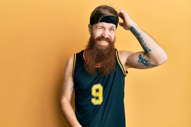 Basketbol forması giyen uzun sakallı kızıl saçlı adam soru sorup şaşırıyor. Şüpheyle kararsız, kafa kafaya düşünerek. Düşünceli kavram. 