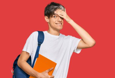 Sırt çantası takan, elinde kitap tutan, kafası karışmış, şaşırmış ve kızgın yüzlü İspanyol bir genç. 