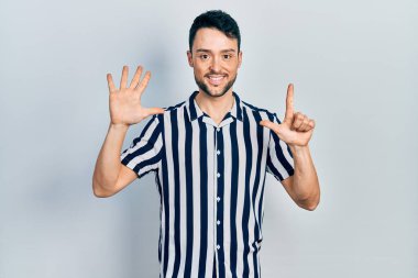 Gündelik kıyafetler giyen genç İspanyol adam yedi numarayı gösterip işaret ederken kendinden emin ve mutlu bir şekilde gülümsüyor.. 