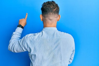 Gündelik giysiler ve gözlük takan genç İspanyol adam, parmak eliyle öne doğru poz veriyor. 