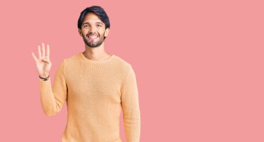 Yakışıklı İspanyol adam gündelik süveter giyer ve parmaklarıyla dört numarayı gösterirken kendinden emin ve mutlu bir şekilde gülümser.. 