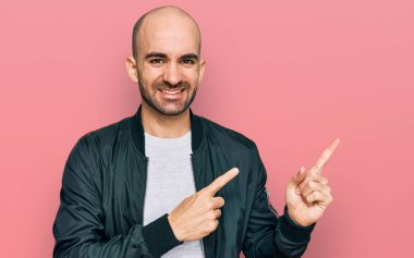 Gündelik kıyafetler giyen genç İspanyol adam gülümseyip kameraya bakıyor ve iki eliyle ve parmaklarıyla kenarı işaret ediyor.. 