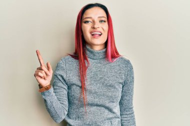 Gündelik kıyafetler giyen genç beyaz kadın bir numarayı gösterip işaret ederken kendinden emin ve mutlu bir şekilde gülümsüyor.. 