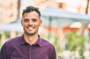 Genç İspanyol adam gülümseyerek şehirde mutlu mesut dikiliyor..