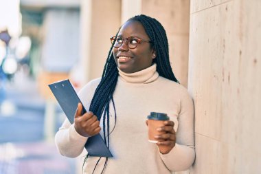 Genç Afro-Amerikalı kadın elinde dosya ve içki ile şehirde kahve içiyor..