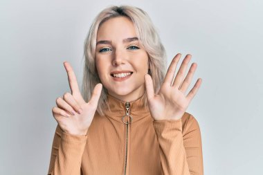 Genç sarışın kız gündelik kıyafetler giyer ve yedinci parmaklarını göstererek gülümserken kendinden emin ve mutluydu.. 