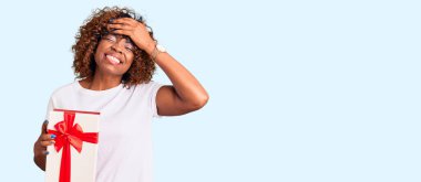 Genç Afro-Amerikalı kadın elinde hediye tutarken elleri havada, şaşırmış ve sinirli bir halde. 