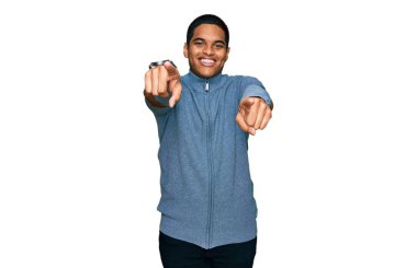 Gündelik kazak giyen genç, yakışıklı İspanyol adam seni ve kamerayı işaret ediyor, pozitif ve neşeli gülümsüyor. 