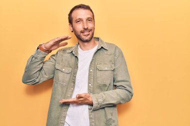 Elleriyle el kol hareketi yapan, büyük ve büyük beden işareti gösteren sıradan kıyafetler giyen genç yakışıklı bir adam. Kameraya bakıp gülümsüyor. ölçüm kavramı. 