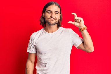 Gündelik kıyafetler giyen, gülümseyen, kendine güvenen, el hareketleriyle küçük boy işareti yapan, parmaklarıyla işaret eden ve kameraya bakan genç yakışıklı bir adam. ölçüm kavramı. 
