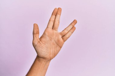 Beyaz bir gencin kolu ve eli pembe izole edilmiş arka planda Vulkan selamı veriyor, el ve parmaklarını gösteriyor, ucube kültürü sergiliyor. 