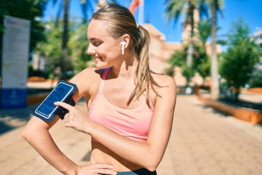 Genç sarışın sporcu. Parkta egzersiz yaparken kulaklık takıyor..