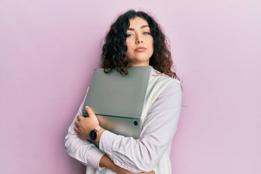 Kıvırcık saçlı, laptopa sarılan, sevgiyle sarılan esmer bir kadın. Yüzünde ciddi bir ifadeyle rahatlamış. Basit ve doğal bir şekilde kameraya bakıyorsun.. 