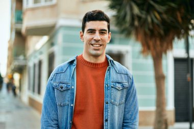 Genç İspanyol adam gülümseyerek şehirde mutlu mesut dikiliyor..