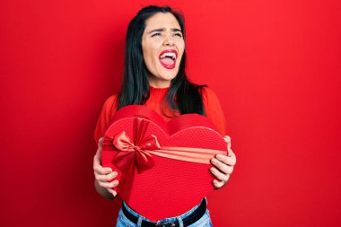 Sevgililer günü hediyesini elinde tutan genç İspanyol kız kızgın ve kızgın bağırıyor öfkeyle bağırıyor. öfke ve agresif konsept. 