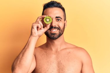 İspanyol asıllı genç üstsüz bir adam elinde kivi tutuyordu. Olumlu ve mutlu görünüyordu. Kendine güvenen bir gülümsemeyle duruyordu. 