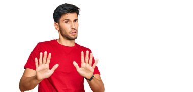 Young handsome man wearing casual red tshirt moving away hands palms showing refusal and denial with afraid and disgusting expression. stop and forbidden. 