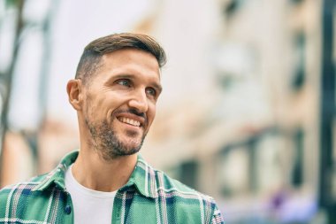 Genç beyaz adam gülümseyerek şehirde mutlu mesut duruyor..