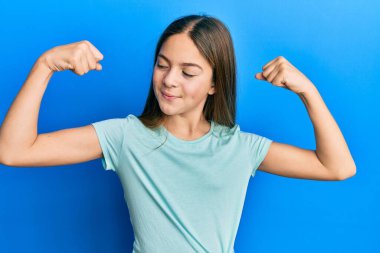 Güzel esmer, beyaz tişört giyen küçük bir kız. Kollarında gururla gülümseyen kaslar var. fitness konsepti. 