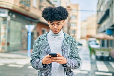 Şehirdeki akıllı telefonu kullanarak ciddi bir ifade takınan genç Afro-Amerikan iş adamı..