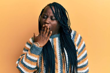 Saçları örülü, günlük kış süveteri giyen genç siyahi kadın ağzıyla ağzını kapatmaktan sıkılmış. Huzursuz ve uykulu.. 