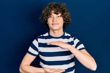 Yakışıklı, sıradan çizgili tişört giyen, elleri büyük ve büyük bir işaret gösteren, ölçü sembolü olan genç bir adam. Kameraya bakıp gülümsüyor. ölçüm kavramı. 