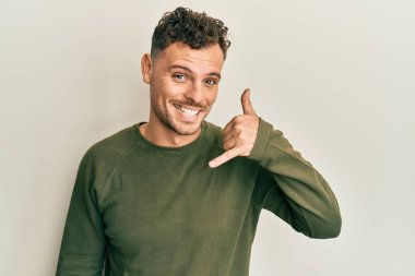 Günlük kıyafetler giymiş, gülümseyen genç İspanyol adam telefonla el ve parmak hareketleri yapıyor telefonda konuşur gibi. iletişim kavramları. 