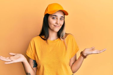 Teslimat üniforması giyen, şapkasız, elleri ve kolları havada, kafası karışmış genç İspanyol bir kadın. şüphe kavramı. 