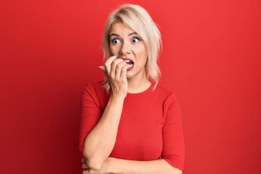 Günlük kıyafetler giyen genç sarışın kız gergin ve gergin görünüyor. Ağzı tırnak yiyen ellerle. anksiyete. 