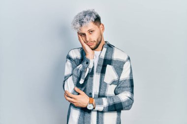 Modern boyalı saçlı, sıradan tişörtlü, yorgun ve bunalımda kollarını kavuşturmaktan sıkılmış görünen genç bir İspanyol.. 