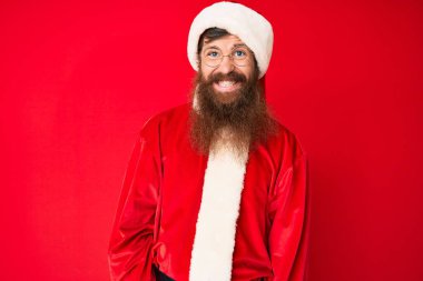 Uzun sakallı, yakışıklı, Noel Baba kostümü giyen yakışıklı genç adam. Pozitif ve mutlu görünüyor. Kendine güvenen bir gülümsemeyle dişlerini gösteriyor. 