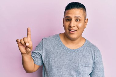 Gündelik kıyafetler giyen genç Latin bir adam bir fikir ya da soruyla gülümsüyor ve mutlu bir yüzle işaret ediyor. 