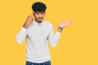 Gündelik kazak giyen genç Arap adam, avuç içi açık fotokopi alanı ve parmak alnına işaret ederek kafasını karıştırmış ve rahatsız etmiş. Bunu bir düşün.. 