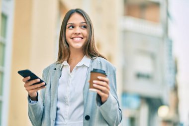 Genç Latin iş kadını akıllı telefon kullanıyor ve şehirde kahve içiyor..