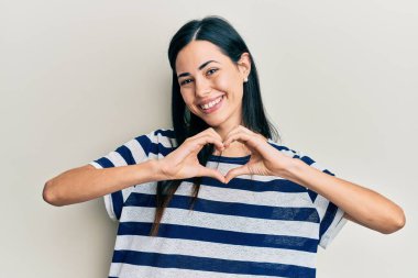 Güzel, genç bir kadın, gündelik giysiler giyip, aşkla gülümsüyor, elleriyle kalp sembolü yapıyor. romantik kavram. 