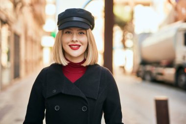 Genç sarışın kadın gülümsüyor, mutlu bir şekilde şehirde duruyor..